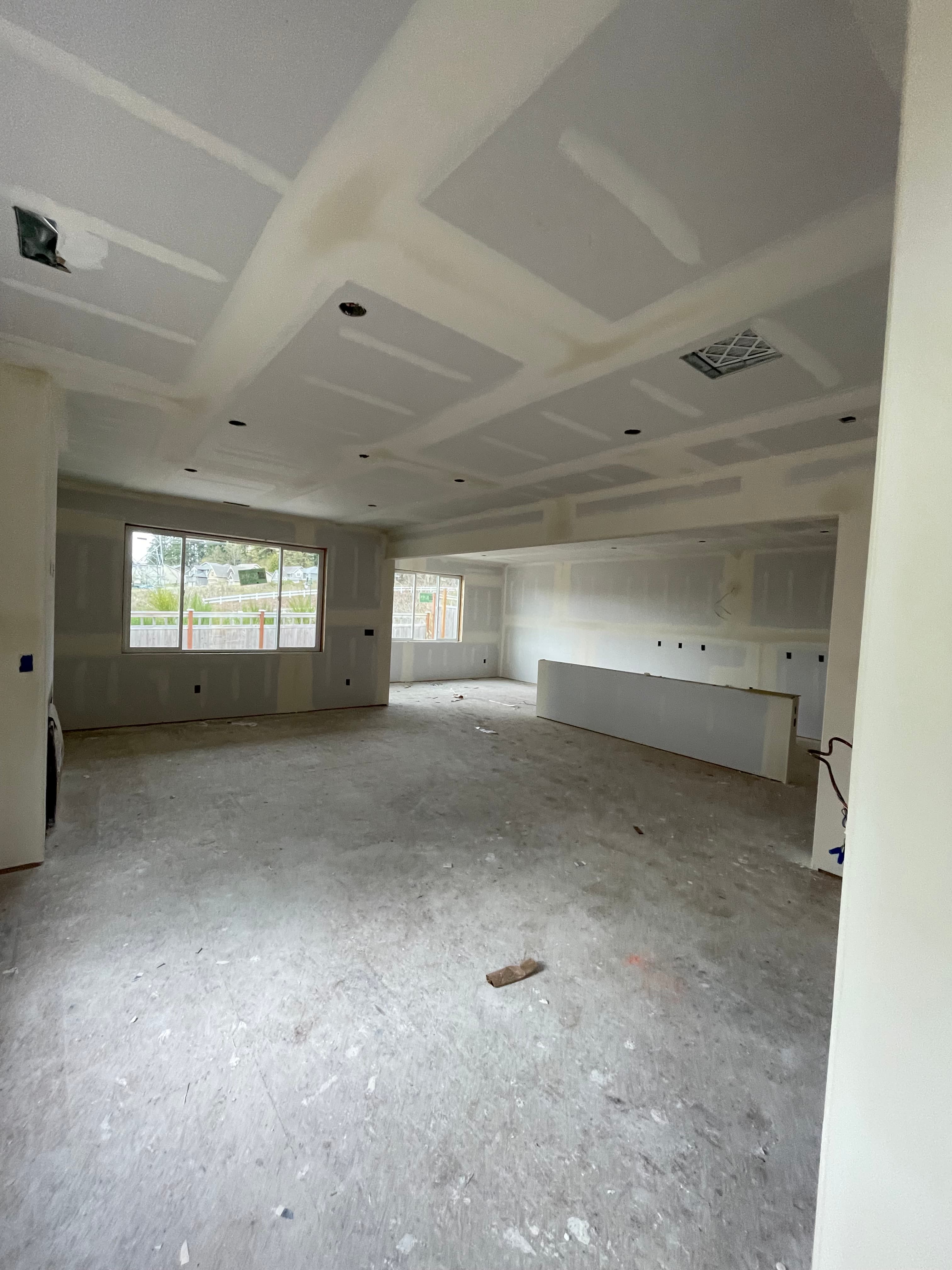 Unfinished interior of a house under construction featuring taped drywall and concrete subfloors.