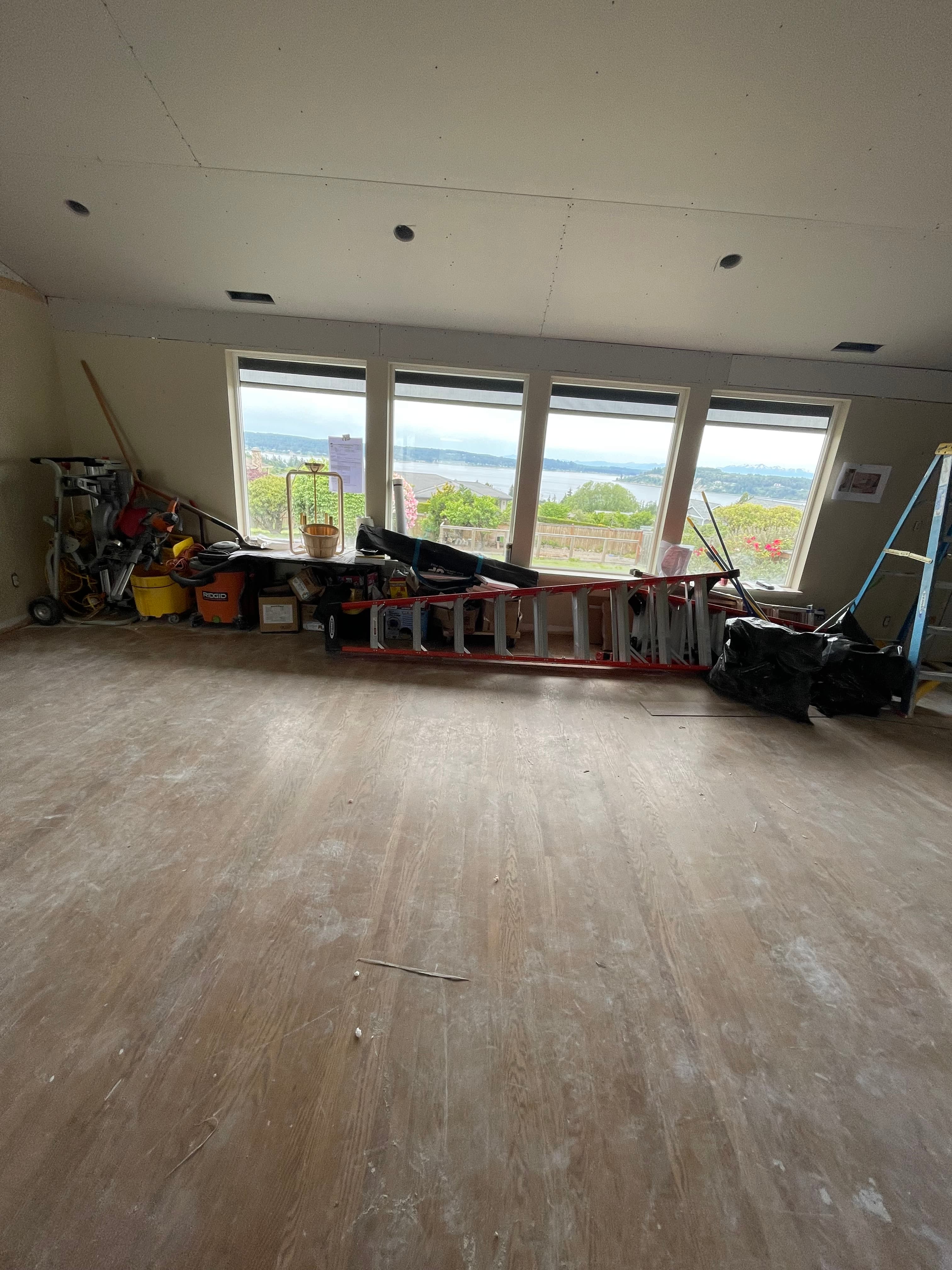 Room under renovation with construction equipment and large windows overlooking a scenic waterfront view.