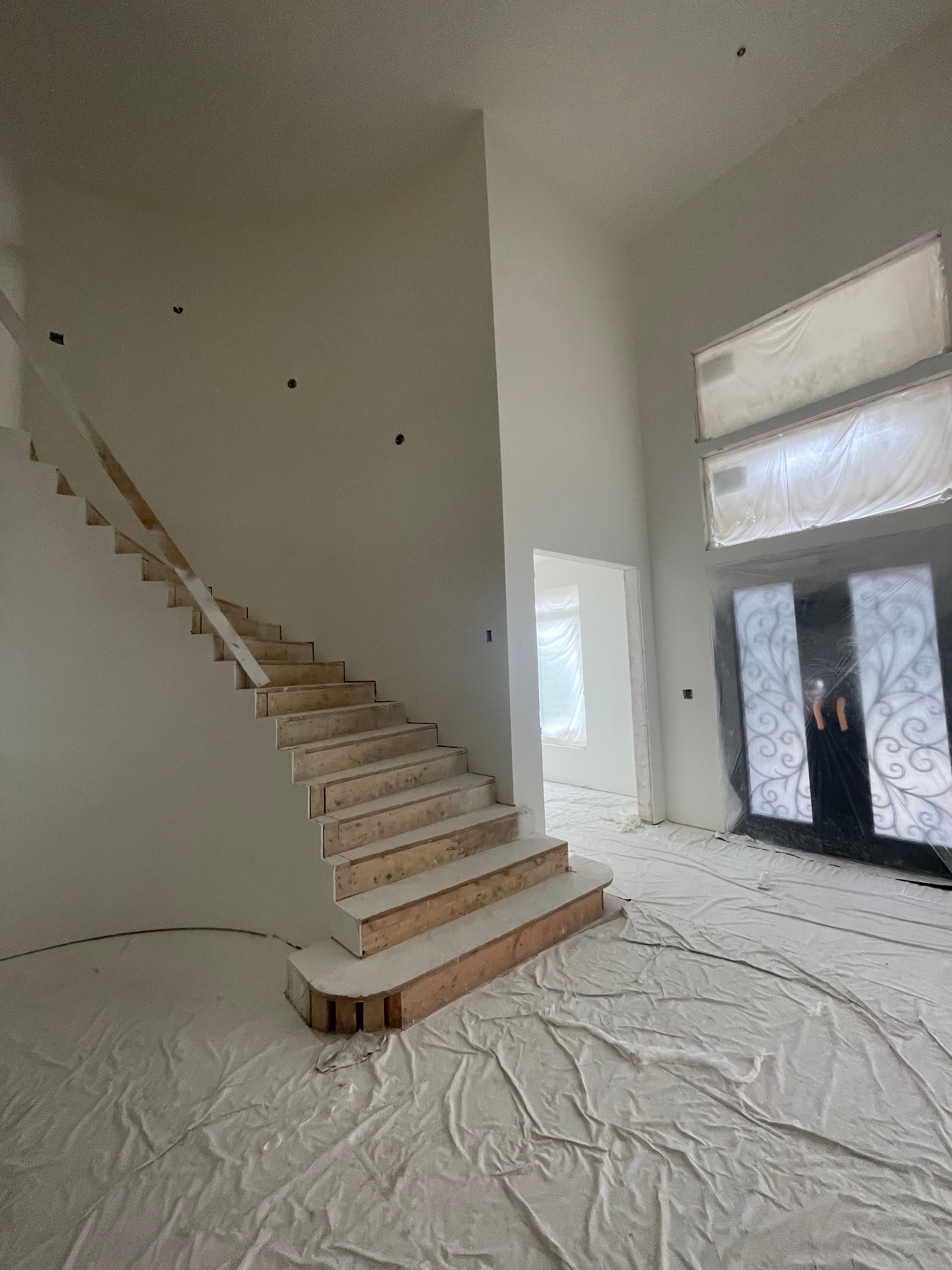 Wooden staircase in a house under construction with white walls and protective floor drop cloths.