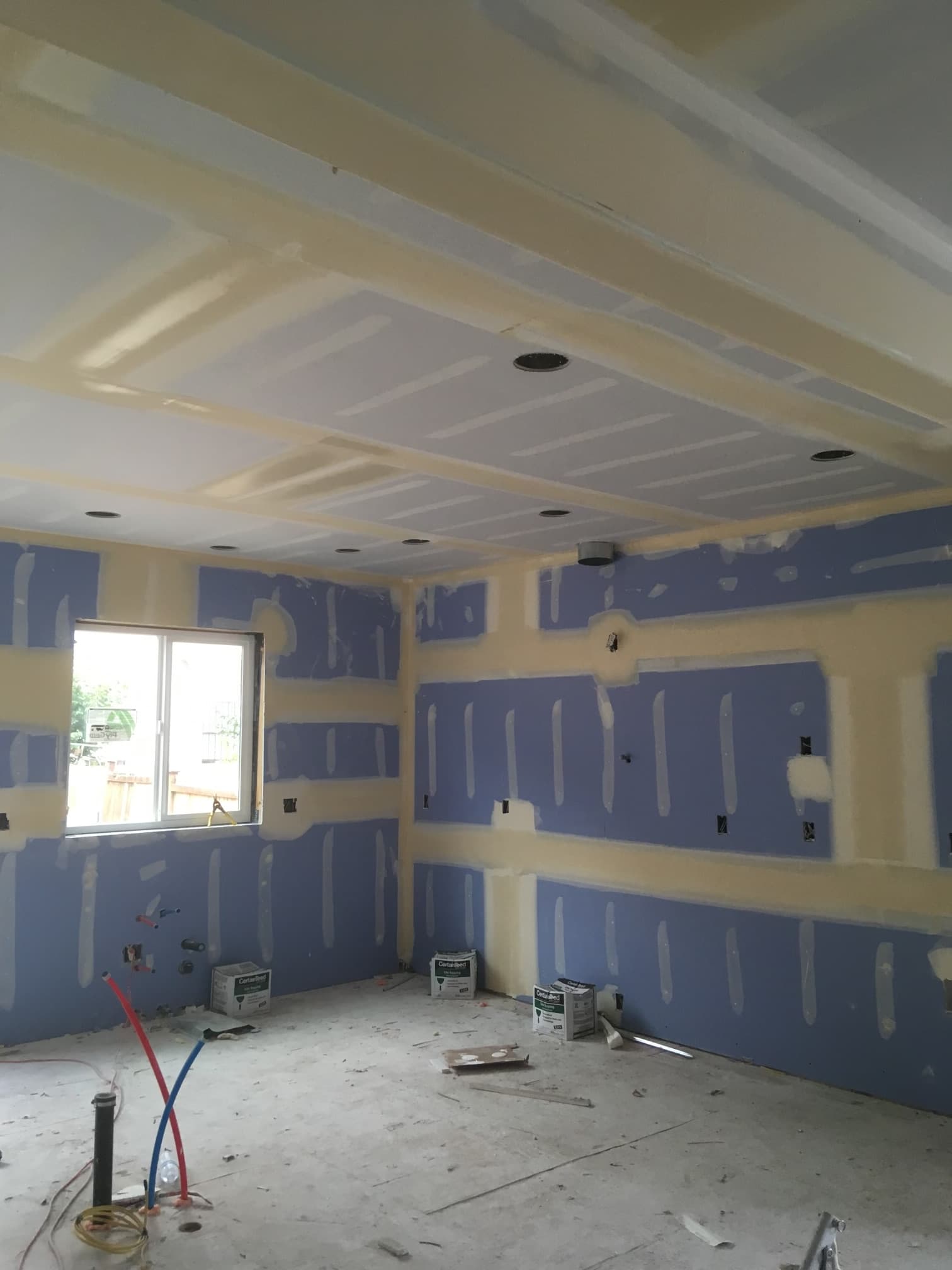 Interior room under construction featuring blue drywall with mudded seams and recessed light cutouts.