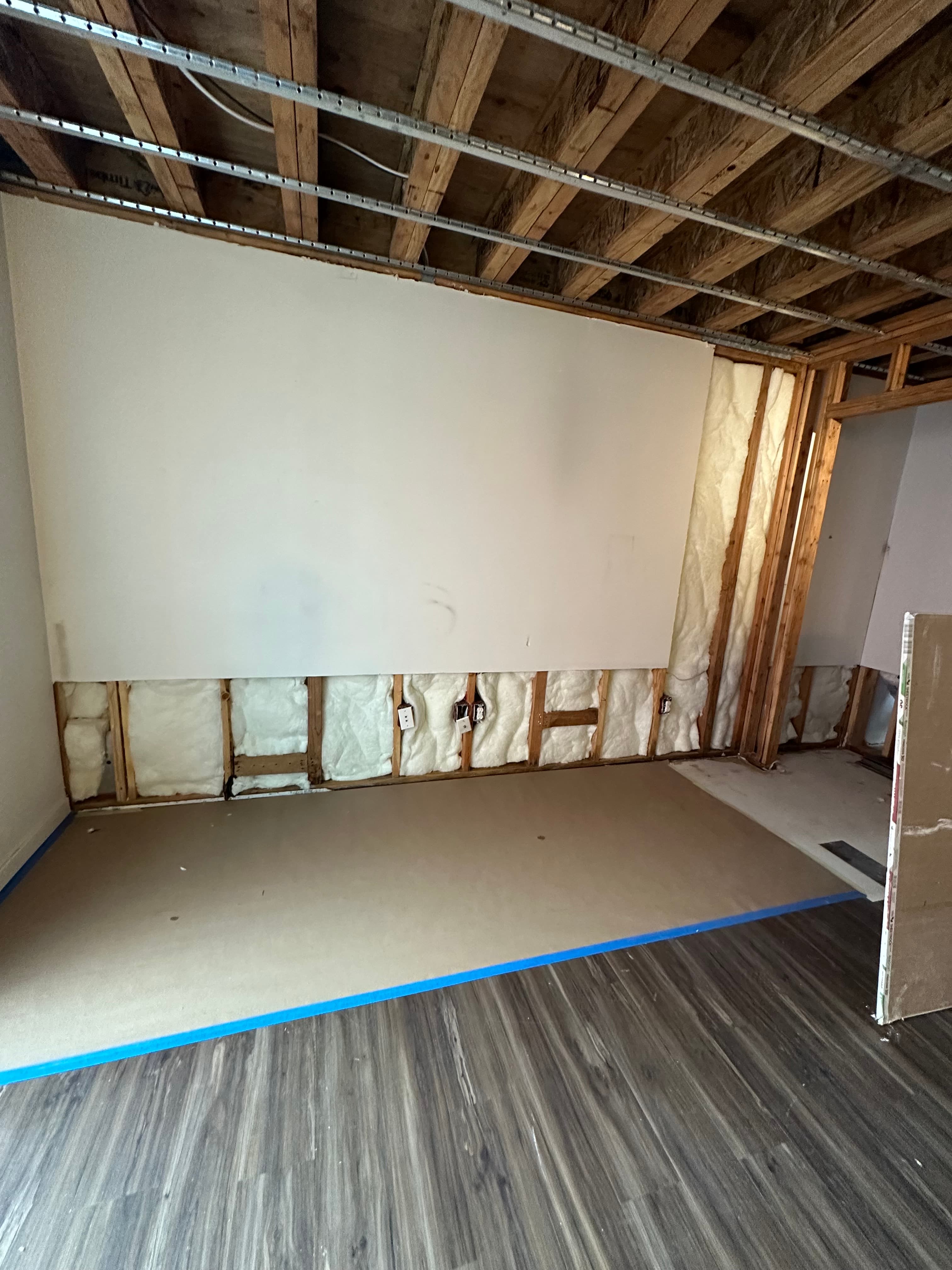 Wooden wall framing with white insulation and a large partially installed drywall sheet.