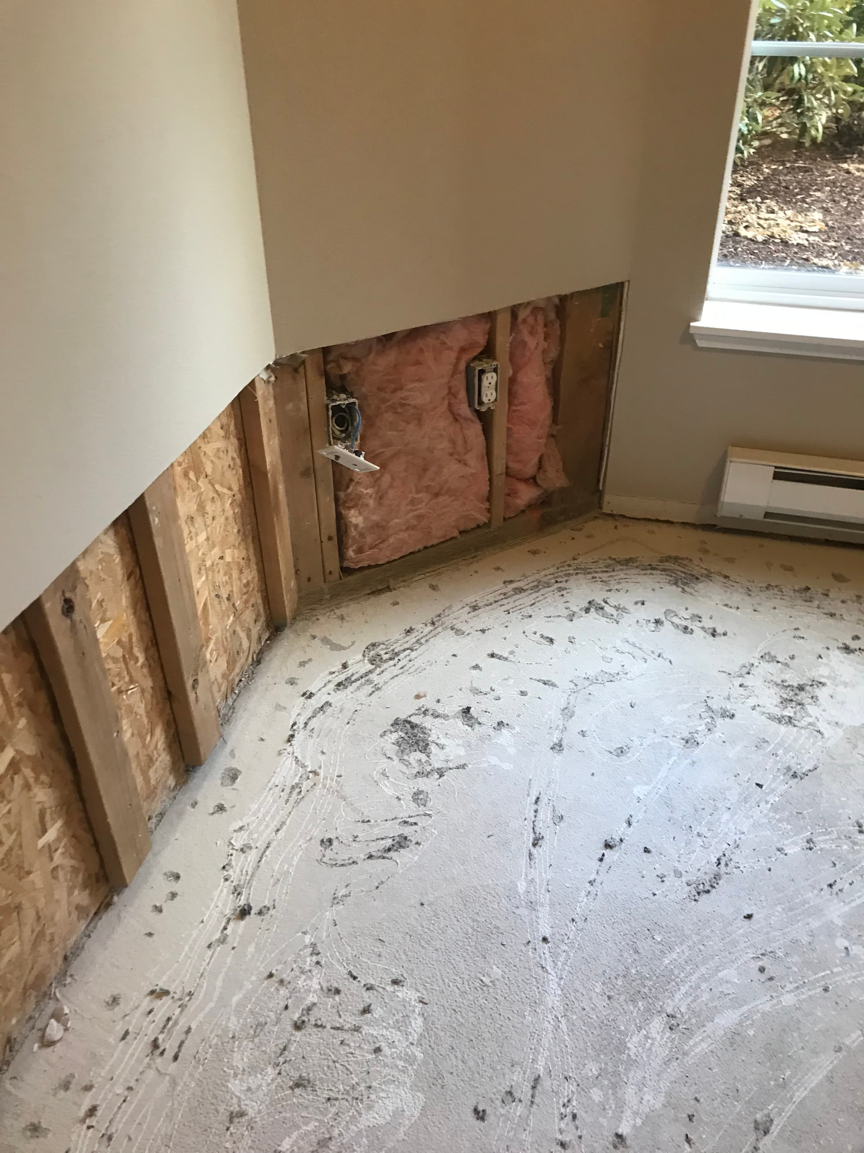 Exposed wall studs and pink insulation in a room with a bare concrete floor.