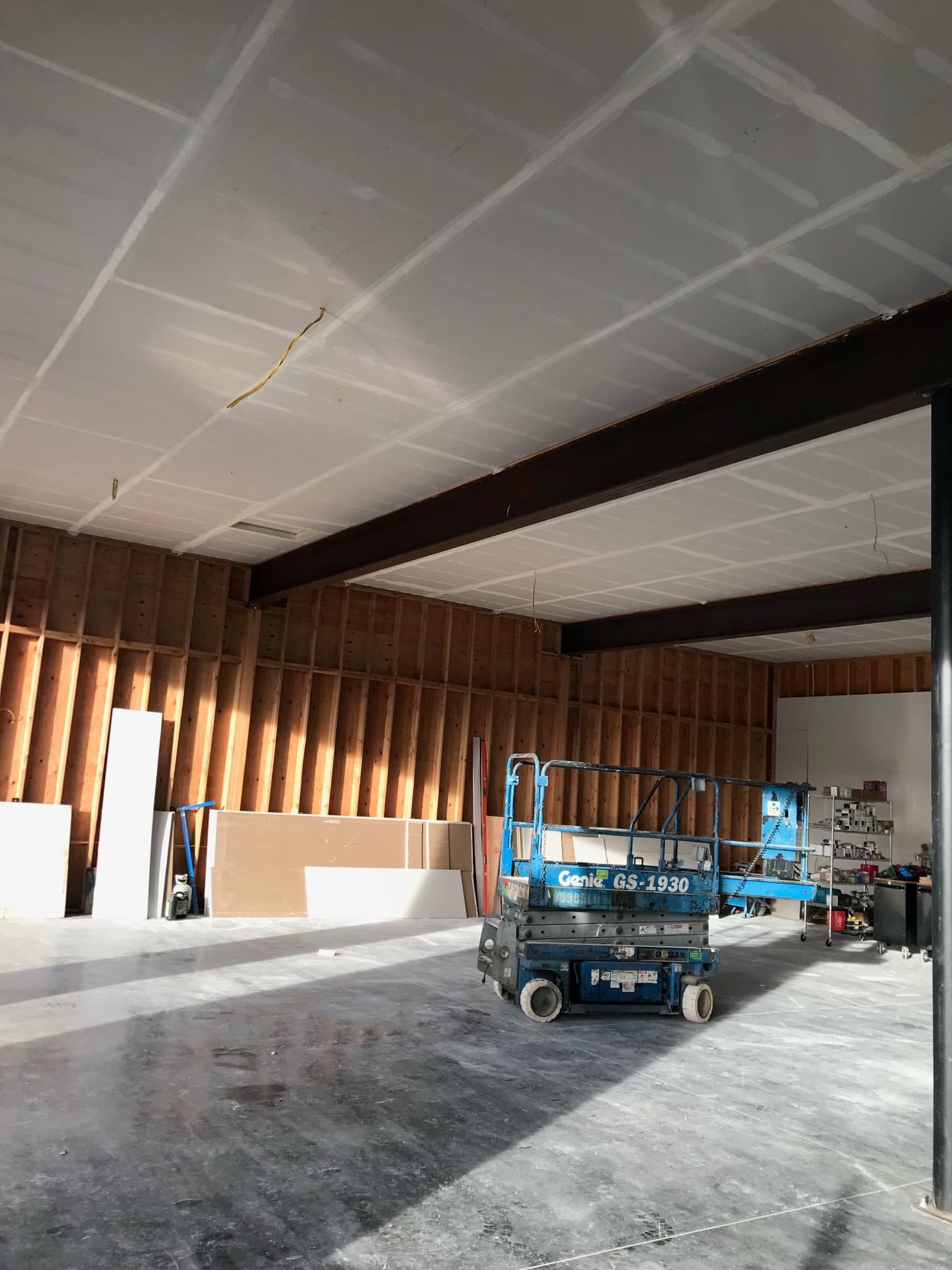 Blue scissor lift parked in a construction site with exposed wooden wall studs and drywall.