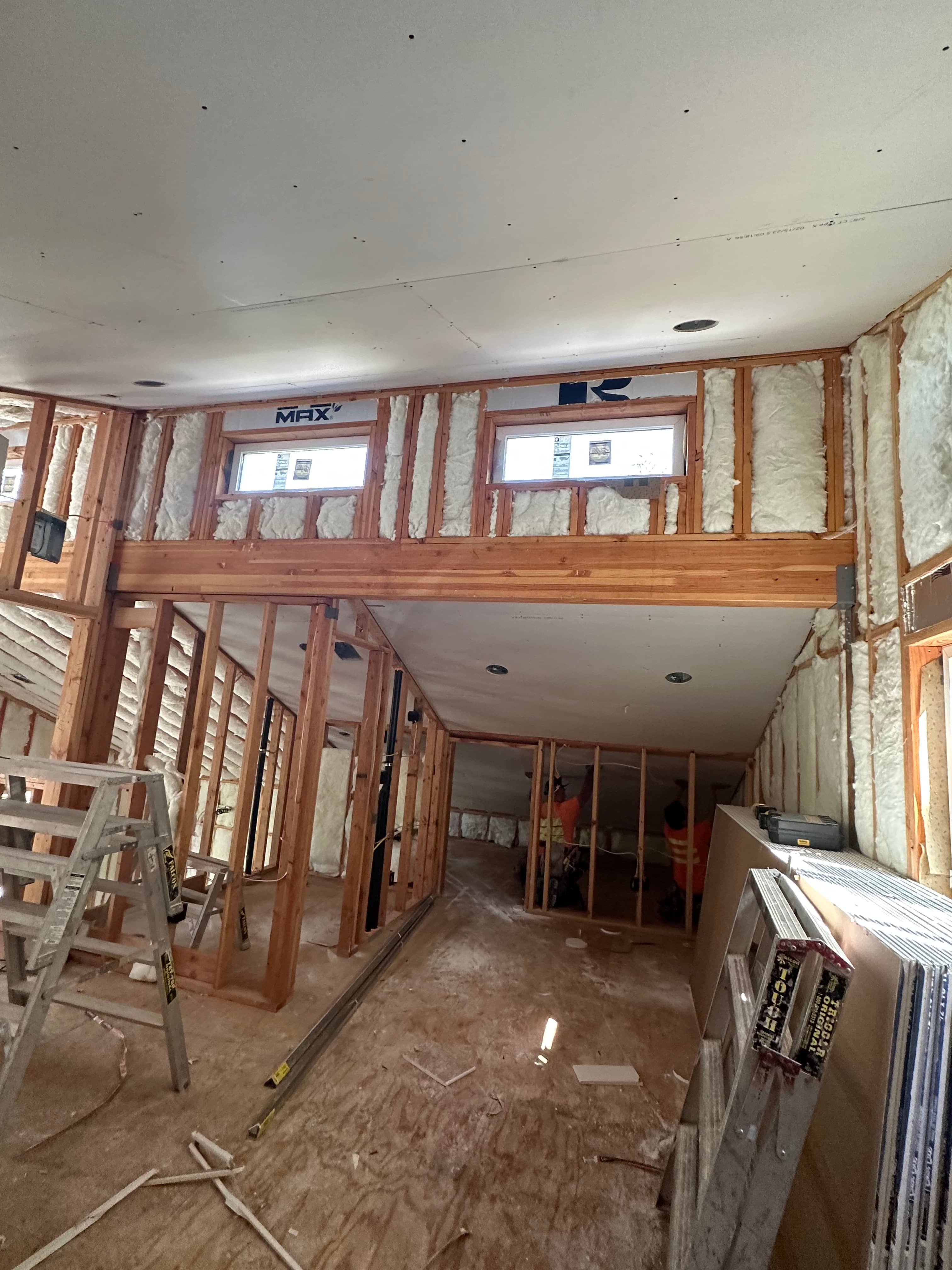 Interior home construction featuring wooden studs, spray foam insulation, and newly installed drywall panels.